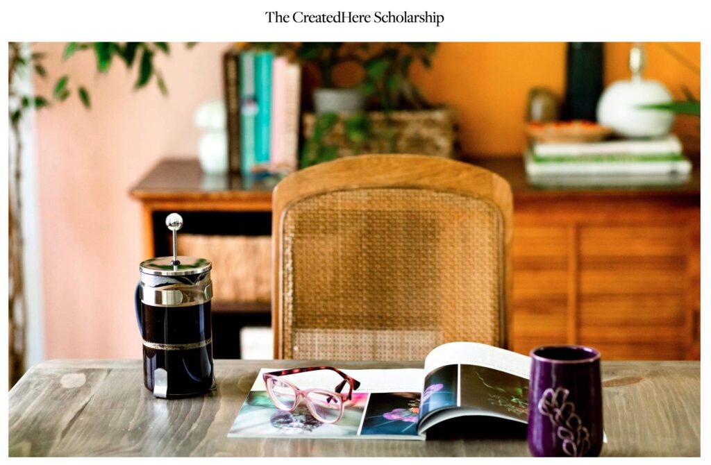 A french press of coffee sits next to an opened copy of CreatedHere magazine, a pair of reading glasses, and a coffee mug. Text reads, the CreatedHere Scholarship.