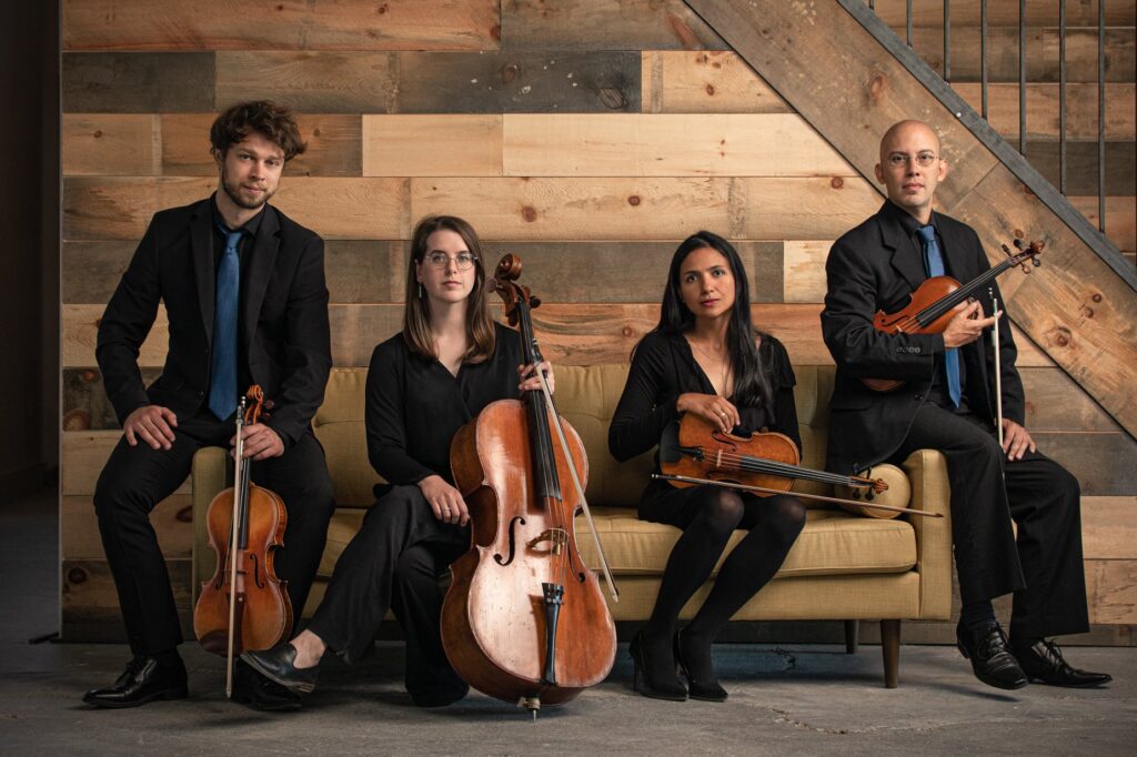 The Elm City String Quartet seated on a couch with their instruments.