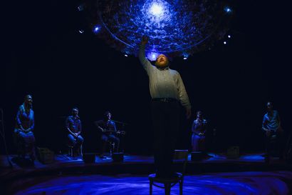 A man stands on a chair, with a light above him.