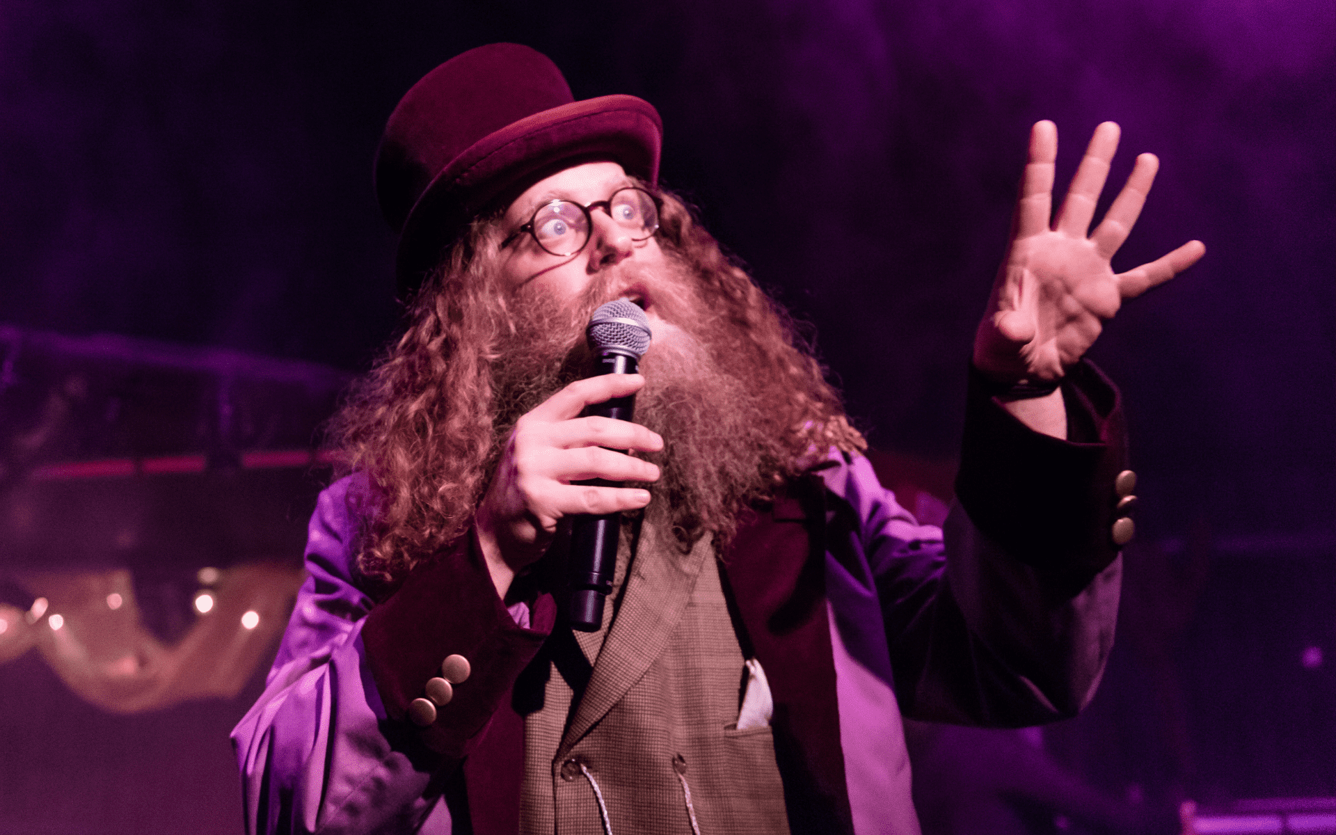 Ben Caplan on stage wearing a purple coat, top hat, and round glasses.