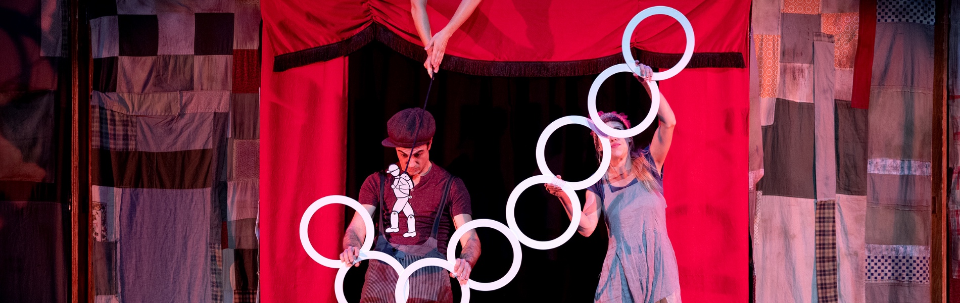 Performers hold rings in front of a red tent.