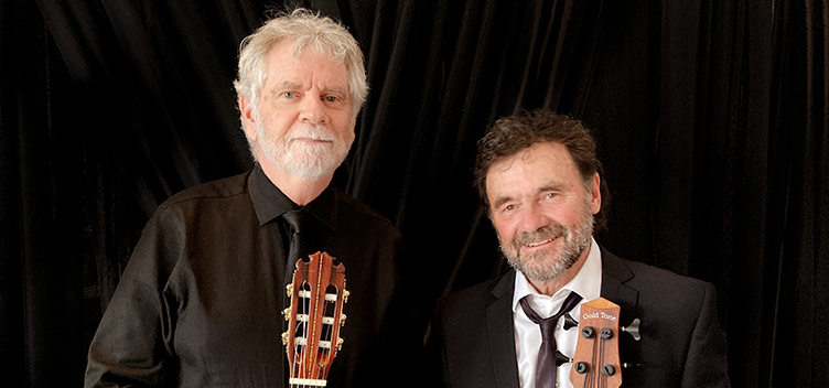 Steven Peacock and Howard Baer dressed in black and holding guitar necks.